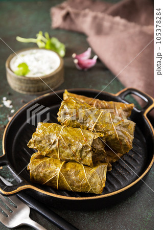 Delicious dolma - stuffed grape leaves with rice and meat on a dark stone background. Traditional Greek, Caucasian and Turkish cuisine. Delicious dolma - stuffed grape leaves with rice and meat on a dark stone background. Traditional Greek, Caucasian and Turkish cuisine. 105378284