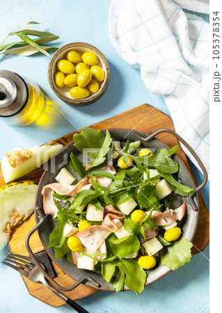 Traditional Spanish and Italian appetizer. Summer mediterranean salad with melon, bacon, olives, white cheese and arugula on blue stone background. View from above. 105378354