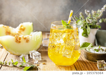 Melon lemonade in glasses with ice and mint on a wooden rustic table. Fresh refreshing fruity summer drink, seasonal beverages. Copy space. 105378364