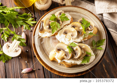 Homemade bruschetta with mushrooms. Toasted sandwich from baguettes bread with soft cheese and grilled mushrooms on wooden rustic table. 105378372