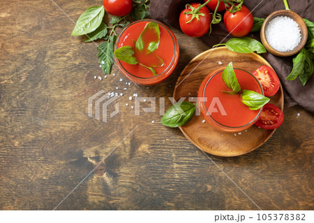 Glasses of fresh tomato juice with tomatoes, salt on wooden table. Vegetable tomato drink for a healthy diet. View from above. Copy space. Glasses of fresh tomato juice with tomatoes, salt on wooden table. Vegetable tomato drink for a healthy diet. View from above. Copy space. 105378382
