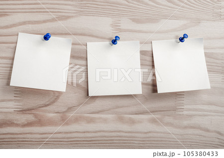 Three white paper notes mockup pinned to wooden bulletin board. sticky notes on bulletin board. Three sticker with push pins on wooden background Three white paper notes mockup pinned to wooden bulletin board. sticky notes on bulletin board. Three sticker with push pins on wooden background 105380433