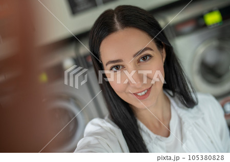 Woman waiting in a laundry room and making selfie on smartphone. Woman waiting in a laundry room and making selfie on smartphone. 105380828