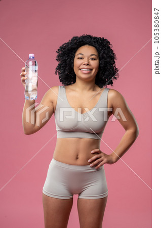 Fit curly-haired woman in lingerie with a bottle of water 105380847