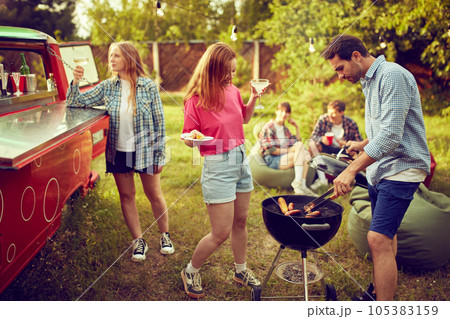Group of young people, friends spending time outdoors, having barbecue party, cooking, drinking cocktails, talking. Countryside meeting 105383159