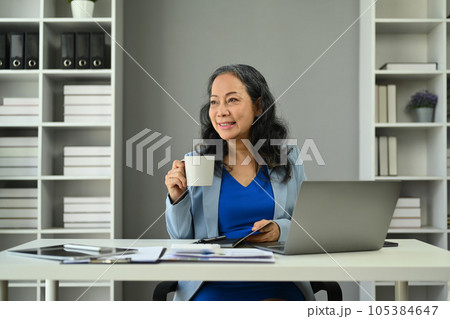 Elegant senior businesswoman manager in trendy suit drinking coffee and looking away  105384647