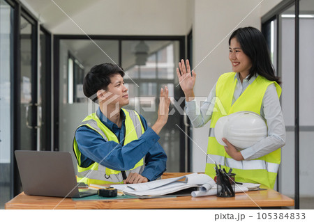 Construction engineer with blueprint making high five while standing on construction site. Home building concept Construction engineer with blueprint making high five while standing on construction site. Home building concept 105384833