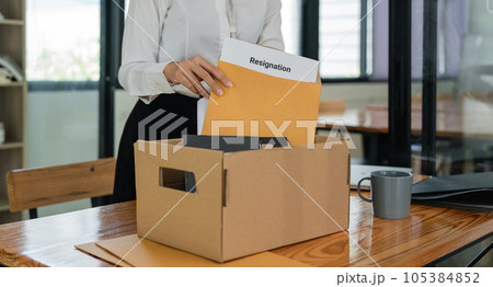 Asian female office worker carrying a cardboard box with her personal stuff and resignation letter Asian female office worker carrying a cardboard box with her personal stuff and resignation letter 105384852