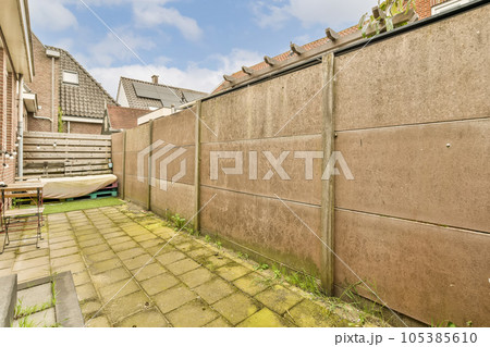 an outside area with a brick wall and green grass in the yard is surrounded by small houses on either sides an outside area with a brick wall and green grass in the yard is surrounded by small houses on either sides 105385610