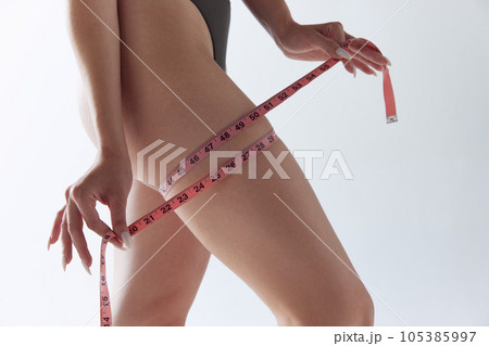 Cropped image of fit young woman in underwear posing measuring leg thigh with measure tape over whitw studio background. 105385997