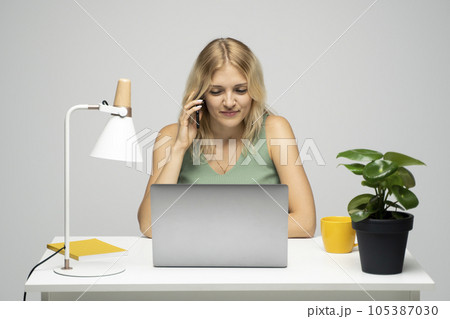Portrait of shiny positive lady dressed green t-shirt and sitting at the table with laptop talking with a phone with a business partner, colleague, friends. 105387030