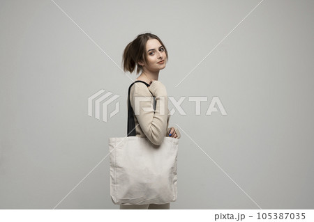 Brunette young girl holding linen shopping bag, mock up. Lady holding flax shopper handbag. Fashion and ecology concept. Brunette young girl holding linen shopping bag, mock up. Lady holding flax shopper handbag. Fashion and ecology concept. 105387035