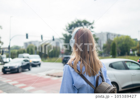 Back view of young blonde Caucasian woman listening the music waiting at traffic lights to cross street 105389427