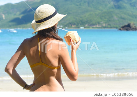 Young woman in yellow swimsuit drinking coconut on a sandy beach 105389656