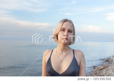 Pretty blonde woman in blue tank top standing on the background of sea and evening cloudy sky Pretty blonde woman in blue tank top standing on the background of sea and evening cloudy sky 105390168