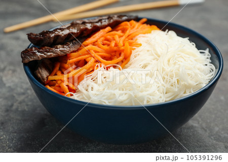Tasty cooked rice noodles with meat and carrot on grey table Tasty cooked rice noodles with meat and carrot on grey table 105391296