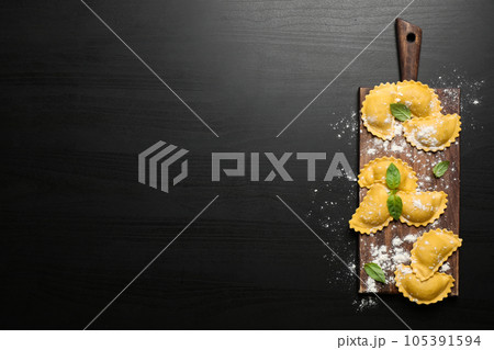 Raw ravioli with basil on black wooden table, flat lay and space for text. Italian pasta 105391594