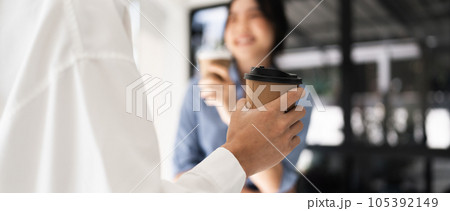 Couple of happy colleagues talking while standing at the office window with cups of coffee 105392149