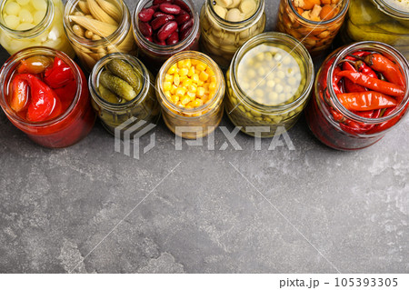 Glass jars with different pickled vegetables on grey table. Space for text 105393305