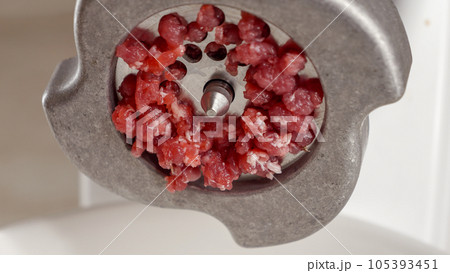 Closeup of minced meat flowing out of meat grinder. Cooking at home, kitchen appliance, healthy nutrition, hamburger ingredients. 105393451