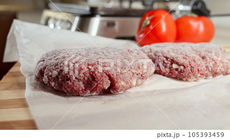 Frozen hamburger patties and ingredients lying on kitchen table next to electric grill. 105393459