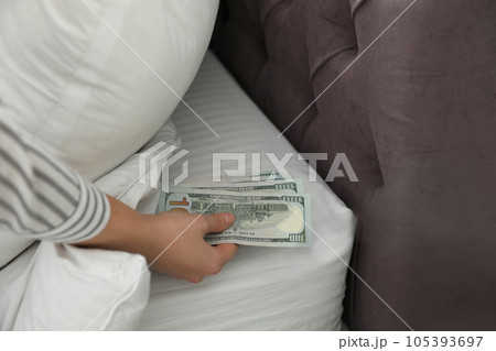 Woman hiding dollar banknotes under pillow in bedroom, closeup. Money savings Woman hiding dollar banknotes under pillow in bedroom, closeup. Money savings 105393697