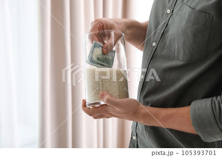 Man hiding money in jar of rice indoors, closeup. Financial savings Man hiding money in jar of rice indoors, closeup. Financial savings 105393701