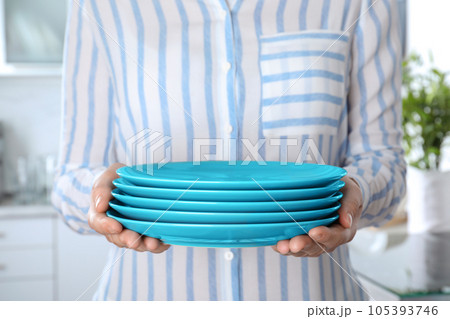 Woman holding stack of clean blue plates in kitchen, closeup Woman holding stack of clean blue plates in kitchen, closeup 105393746