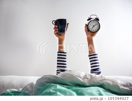 Woman with cup and alarm clock lying in bed, closeup. Morning time 105394027