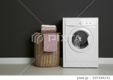 Modern washing machine and laundry basket near black wall Modern washing machine and laundry basket near black wall 105394232