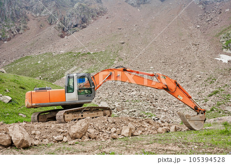 Excavator works in the highlands. Clears the consequences of a mudslide in the gorge of the mountains. repair and expansion of a road Excavator works in the highlands. Clears the consequences of a mudslide in the gorge of the mountains. repair and expansion of a road 105394528
