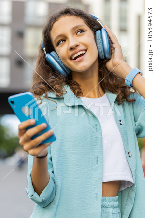 Happy preteen child girl in wireless headphones choosing, listen music dancing outdoors city street 105394573