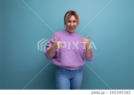 laughing blonde young woman in a lilac sweater with a kind heart on a bright background with copy 105395382