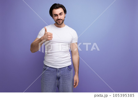 confident young brutal brunette man in a white t-shirt and jeans shows class with his hand confident young brutal brunette man in a white t-shirt and jeans shows class with his hand 105395385