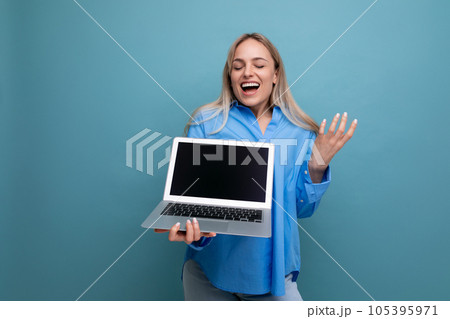 happy lucky blonde girl rejoices with a laptop in her hands with an empty space for a web page on a 105395971