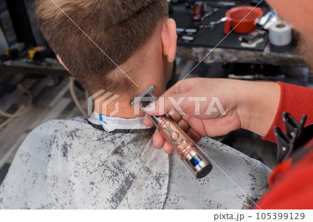 The hand of a professional barber in the process of cutting the back of the head of a client of a young, guy in a salon or hairdresser The hand of a professional barber in the process of cutting the back of the head of a client of a young, guy in a salon or hairdresser 105399129