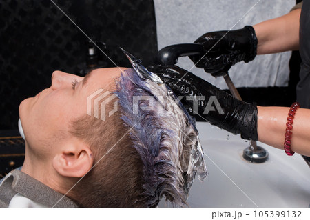 The hands of a girl, a barbershop worker, wearing gloves with rain, water wash off the paint over the sink after dyeing the hair of a client, a guy at work The hands of a girl, a barbershop worker, wearing gloves with rain, water wash off the paint over the sink after dyeing the hair of a client, a guy at work 105399132
