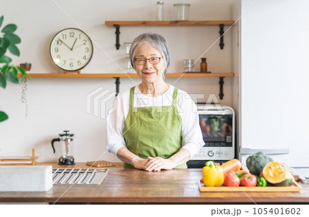 キッチンで野菜を持つエプロン姿の高齢者女性（栄養士・調理師） 105401602