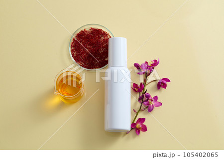 On the beige background, a white cosmetic bottle unbranded decorated with fresh crocus sativus, stigmas saffron and a beaker filled yellow liquid. Cosmetic mockup for advertising and design On the beige background, a white cosmetic bottle unbranded decorated with fresh crocus sativus, stigmas saffron and a beaker filled yellow liquid. Cosmetic mockup for advertising and design 105402065
