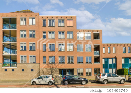 an apartment building with cars parked on the street in front of it and blue sky above, as seen from across the street 105402749