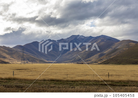 Photograph of a mountain range with grey clouds located behind a large brown agricultural field in New Zealand Photograph of a mountain range with grey clouds located behind a large brown agricultural field in New Zealand 105405458