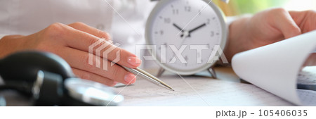 Close up of doctor sitting at desk in clinic with alarm clock and documents. Close up of doctor sitting at desk in clinic with alarm clock and documents. 105406035