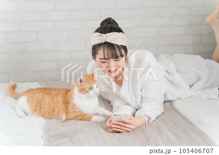 家のベッドルームでペットの猫とスマホで写真を撮って遊ぶアジア人女性 家のベッドルームでペットの猫とスマホで写真を撮って遊ぶアジア人女性 105406707