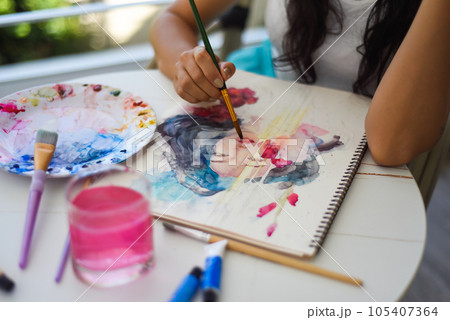 Woman painting watercolor drawing of asian girl with brush on a table with water and paints 105407364