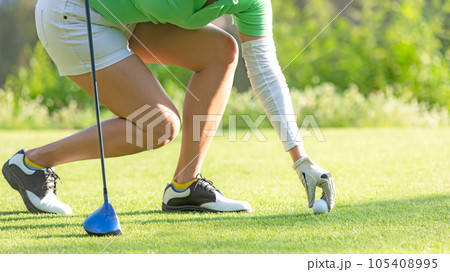 Close up hand asian sporty woman put golf ball on tee with club in golf course on evening on time  105408995