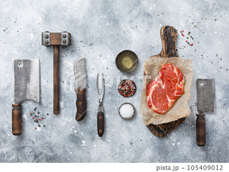 Rib eye steak with meat cleaver,fork,knife with wooden tenderizer and various herb 105409012
