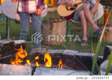 A girl in a plaid shirt roasts marshmallows on a fire in the yard of the house, father plays the guitar. Evening family get-together by the campfire, outdoor picnic in tourist chairs A girl in a plaid shirt roasts marshmallows on a fire in the yard of the house, father plays the guitar. Evening family get-together by the campfire, outdoor picnic in tourist chairs 105409755