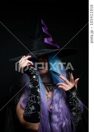 Halloween witch woman in black dress, cloak, black hat with violet ribbon, blue and violet hair and long black nails. 105411916