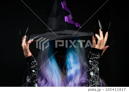 Halloween witch woman in black dress, cloak, black hat with violet ribbon, blue and violet hair and long black nails. 105411917