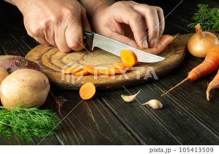 Slicing carrot by the hands of a chef on a cutting board to prepare delicious borscht for lunch at home. 105413509